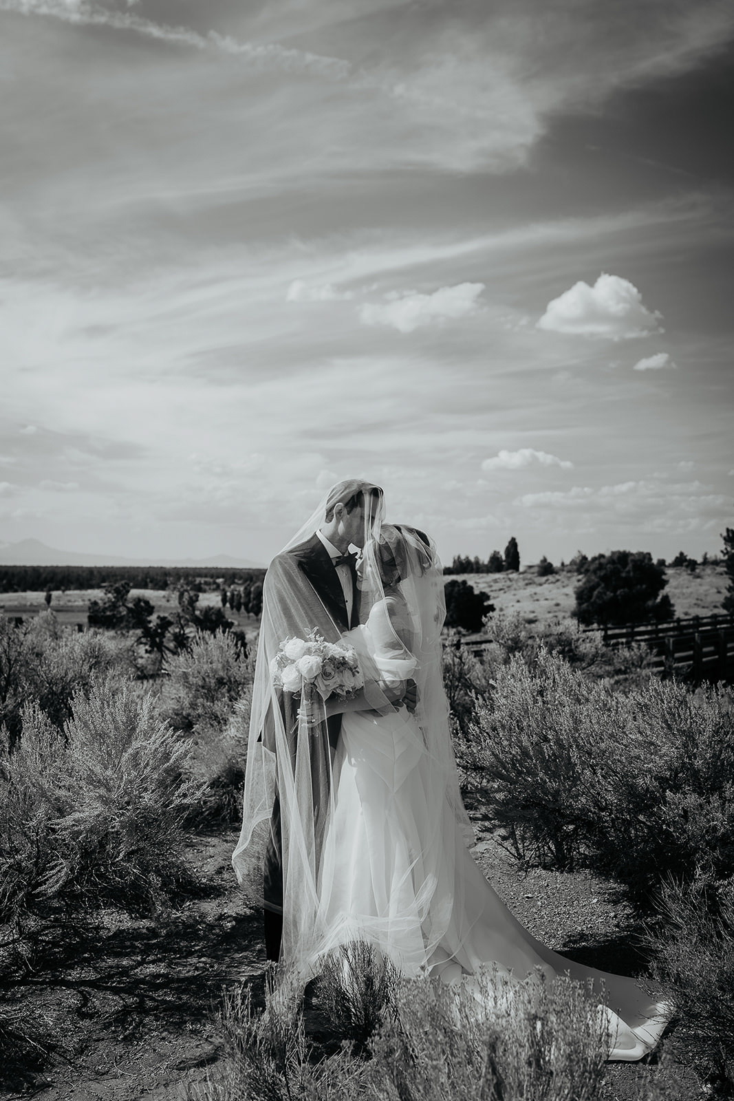 the bride and groom hugging under the bride's veil among brush in the Oregon desert during their Brasada Ranch wedding.