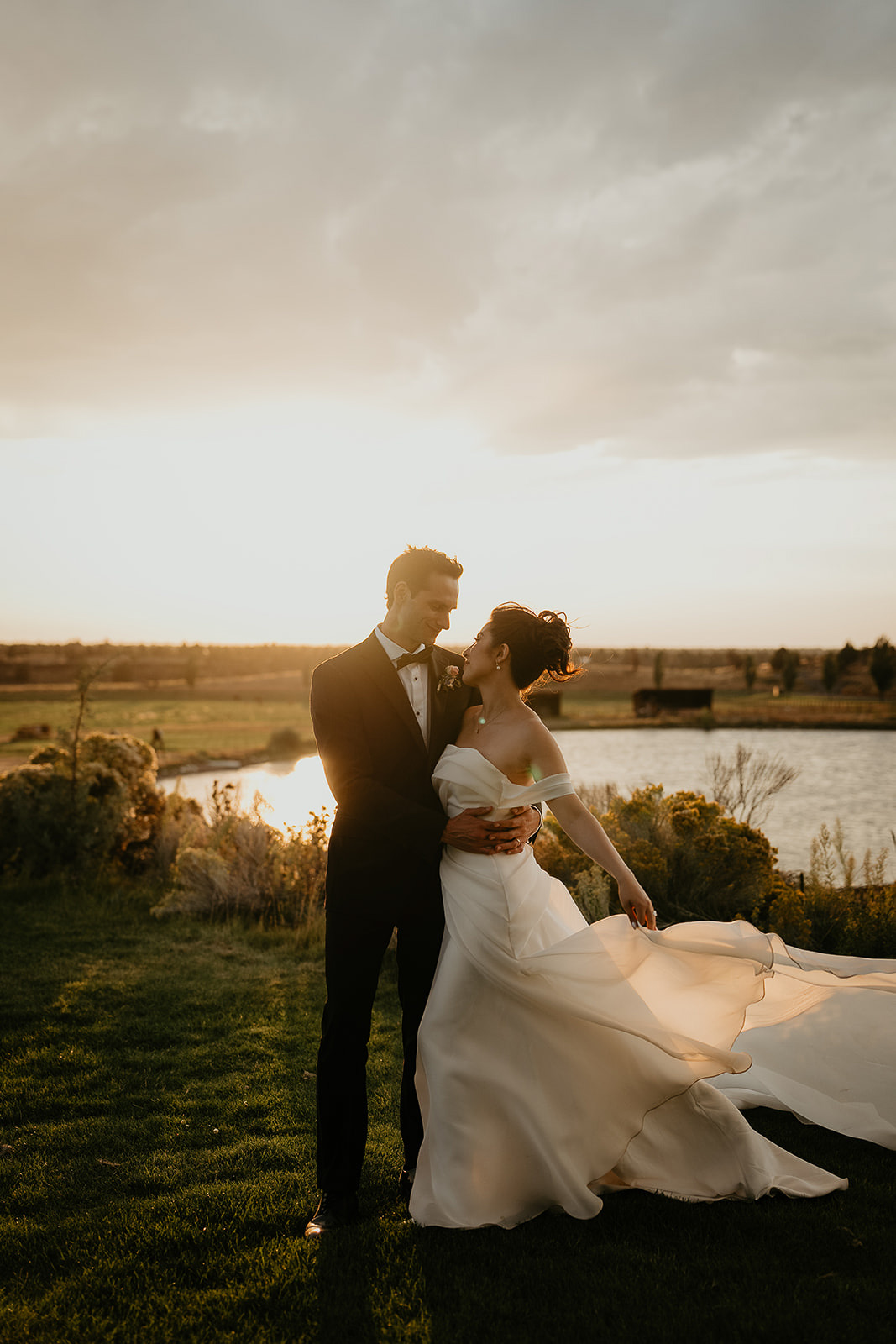 newlyweds holding each other close with a pond and the sunset in the background during their Brasada Ranch wedding.