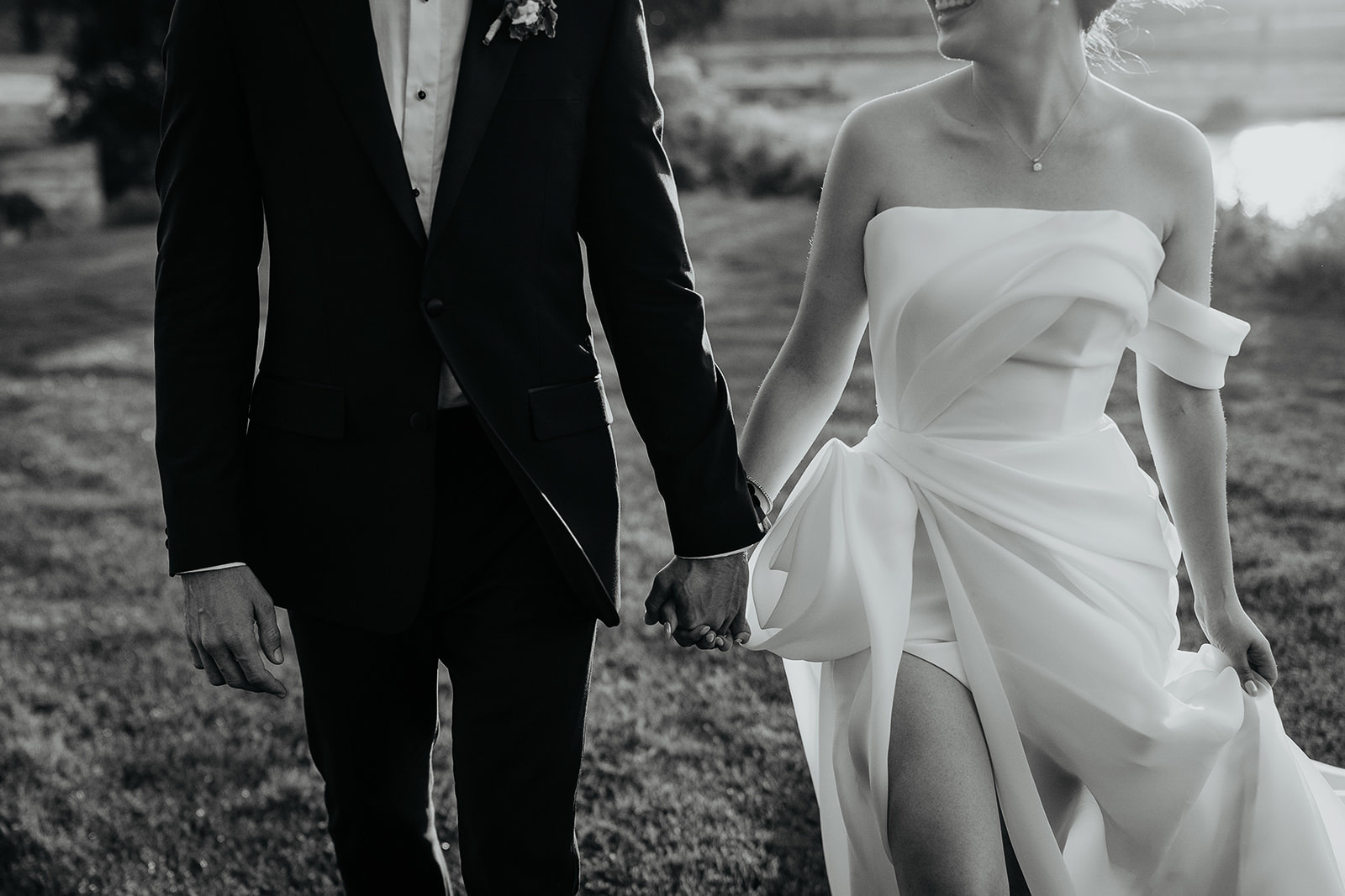 newlyweds holding hands while walking on a grassy field.