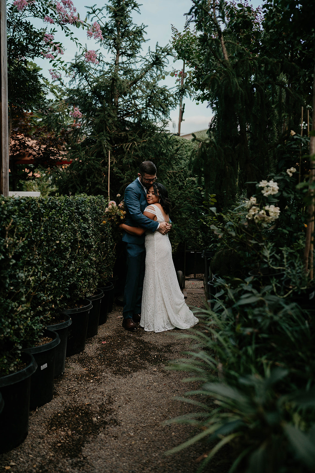 newlyweds hugging next to greenery in a nursery during their Blockhouse wedding venue.