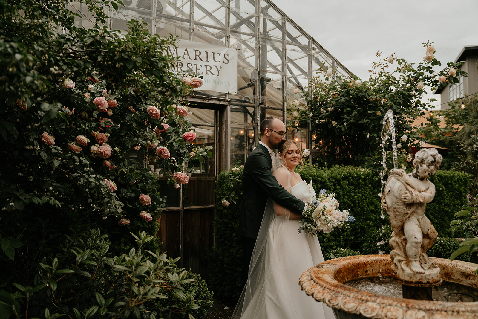 newlyweds hugging next to a fountain by a greenhouse by the Blockhouse wedding venue. 