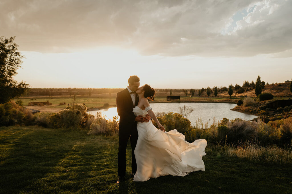 newlyweds kissing at sunset with a pond in the background during their Brasada Ranch wedding.