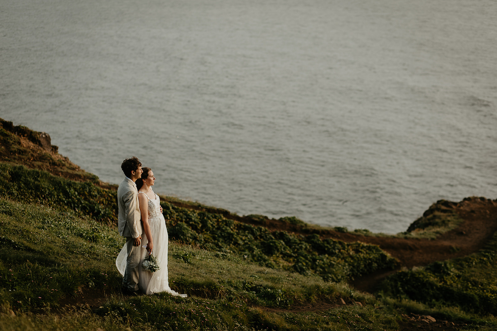 Newlyweds on a cliffside enjoying views of the ocean. 