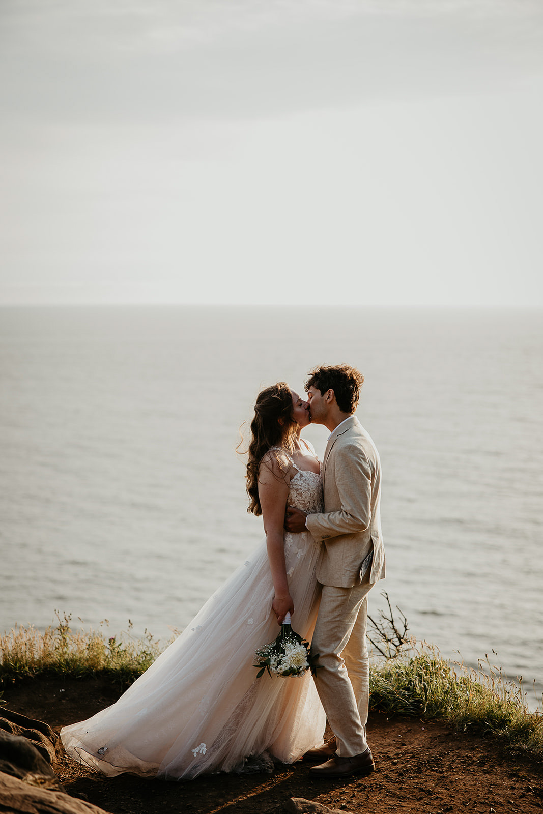 newlyweds kissing on a cliffside above the Oregon Coast.