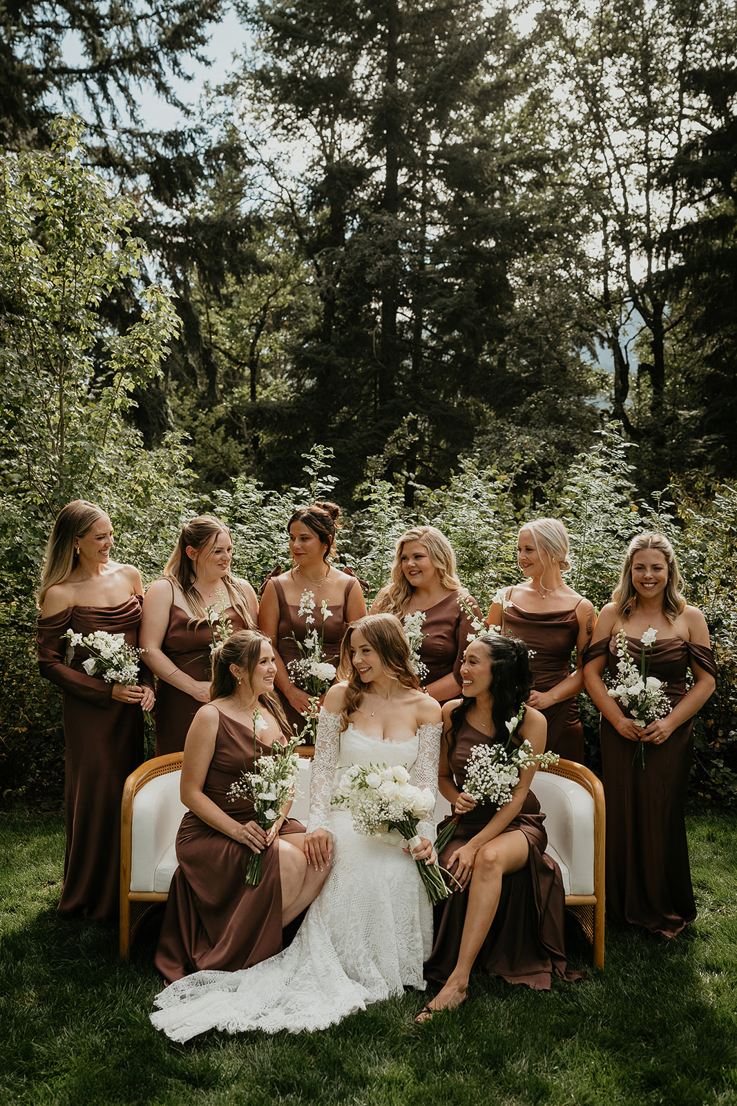 the bride and her bridesmaids on a bench smiling and holding bouquets of flowers.