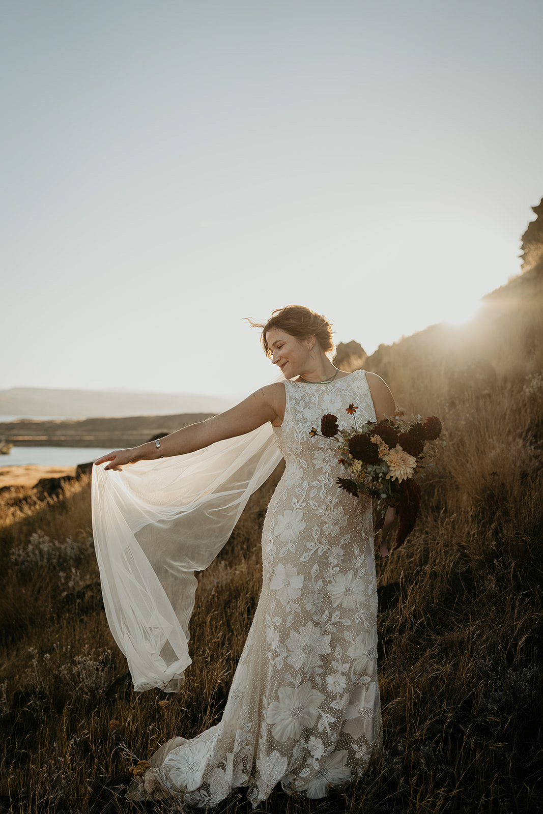 bride holding veil out while standing on golden grass.
