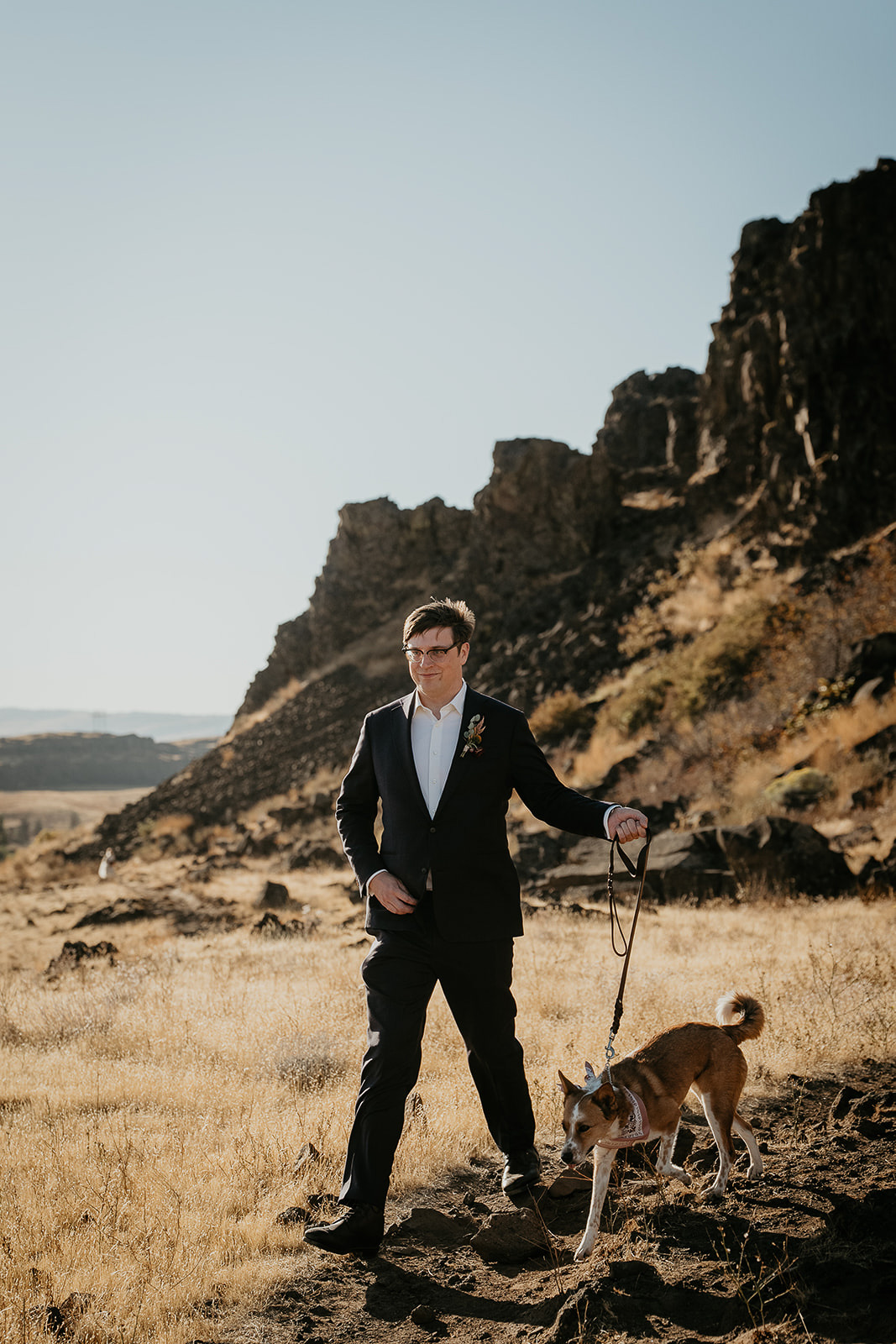 the groom walking on a dirt path with his dog.