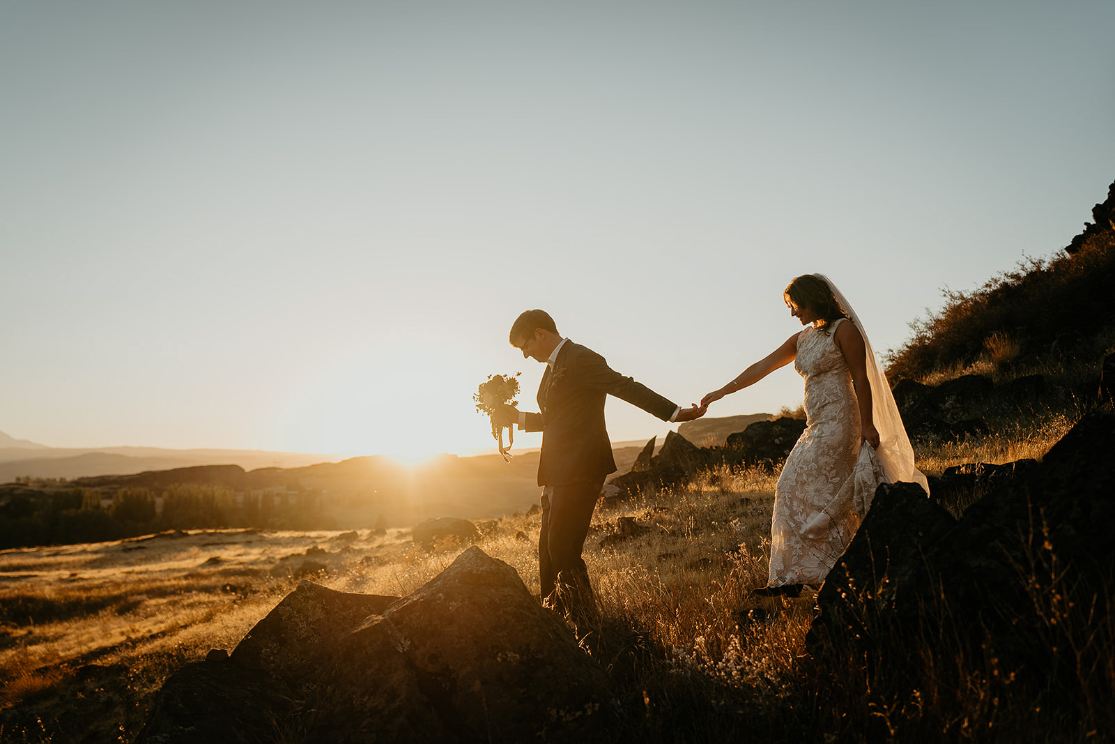 newlyweds holding hands walking through a field of golden grass during their Columbia River Gorge elopement.
