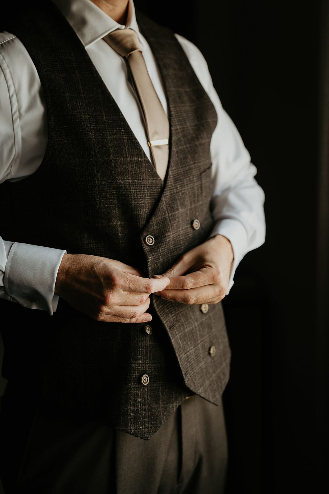 groom buttoning his suit during his forest elopement in Oregon.