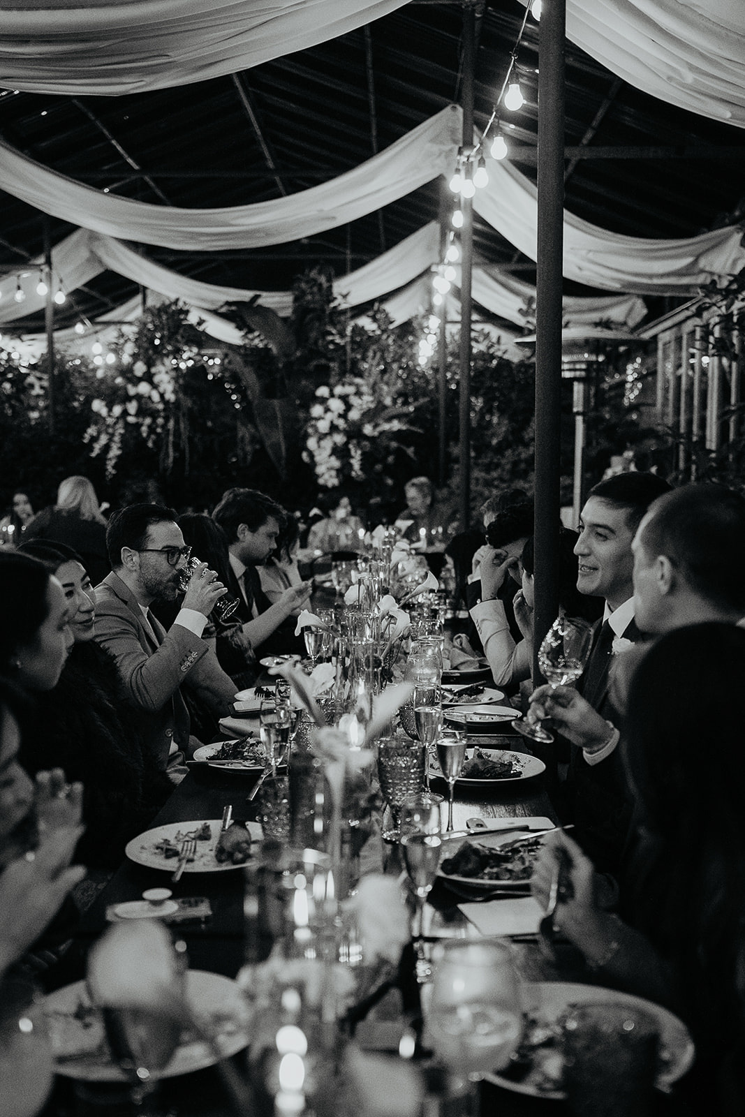 wedding guests enjoying a meal inside a greenhouse converted to a wedding reception area.
