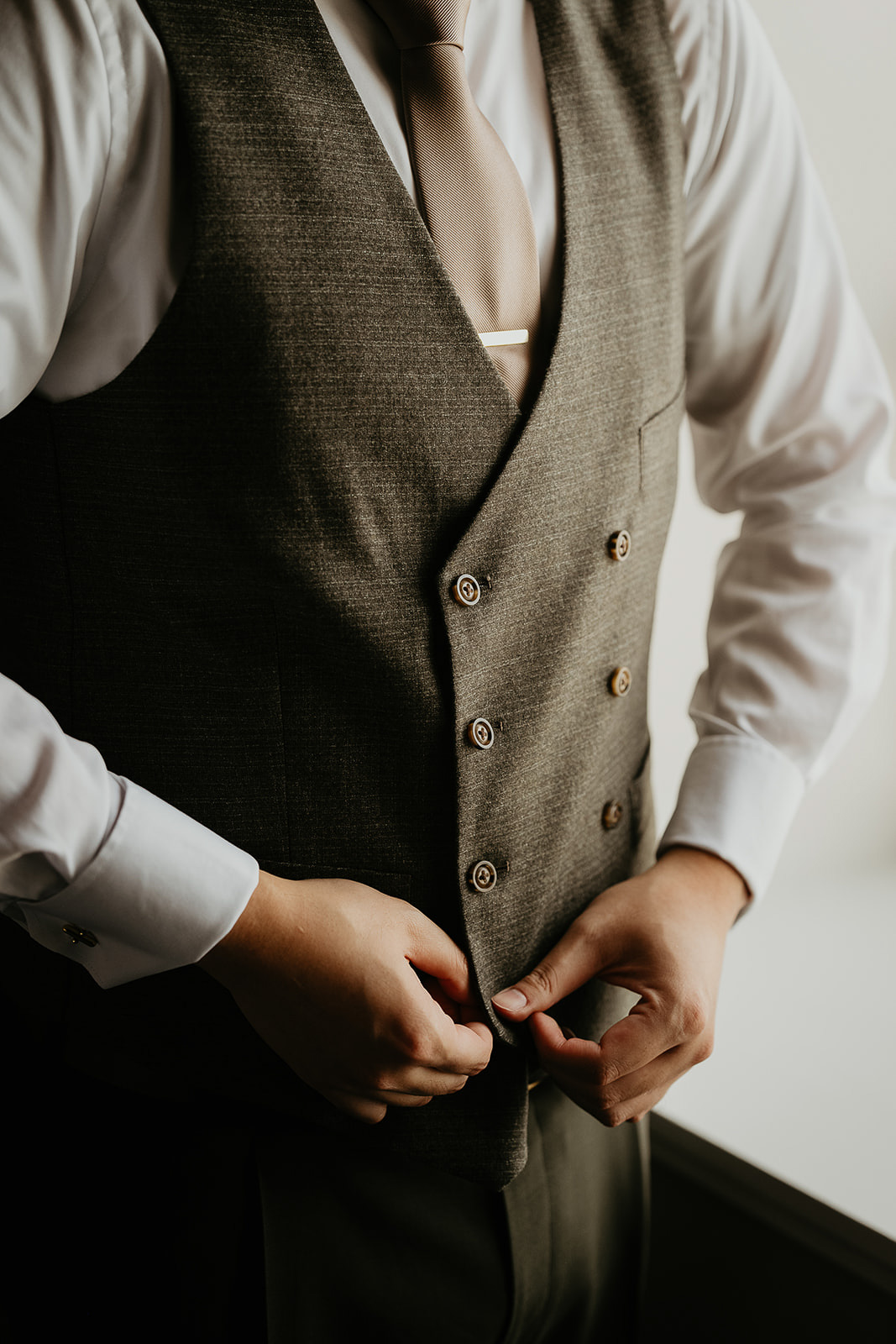 groom buttoning his suit vest.
