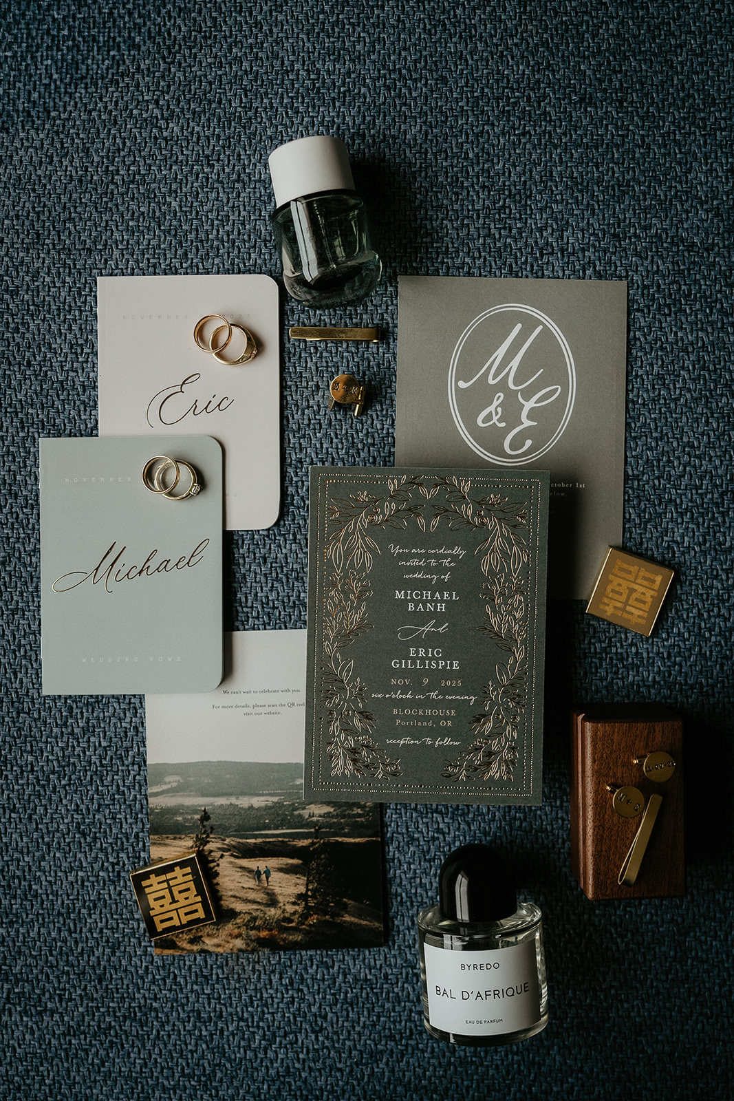 a wedding flat lay including the invite, vows, rings, and cologne.