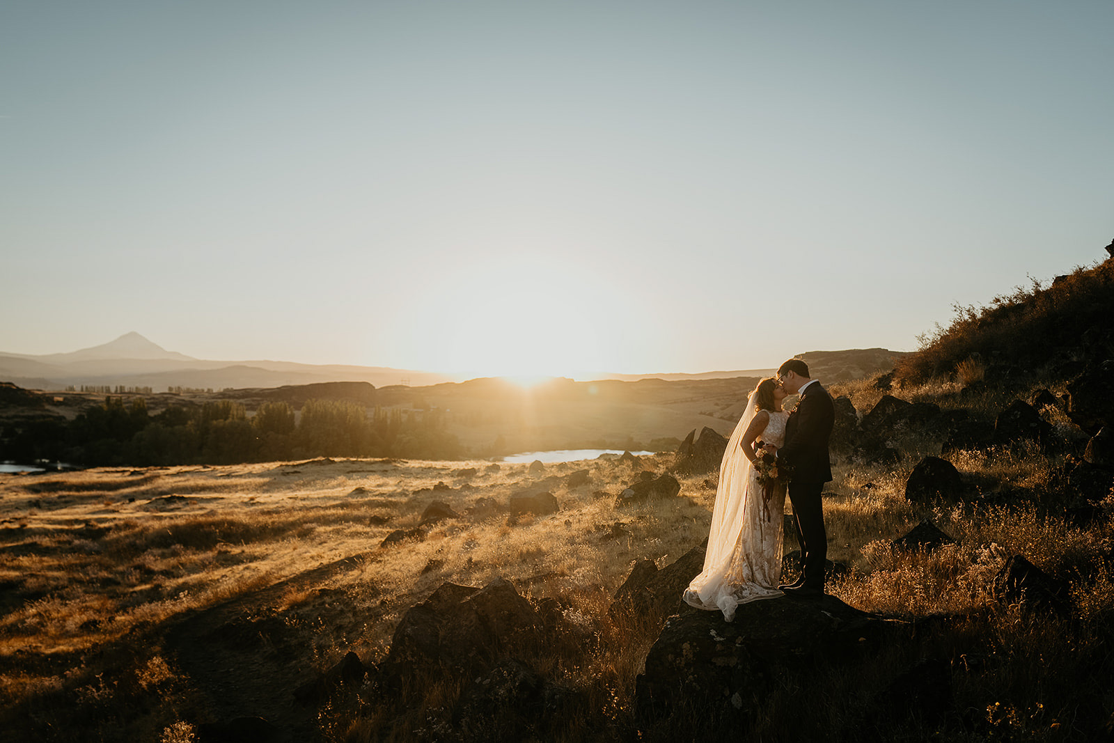 newlyweds kissing at sunset in a meadow.