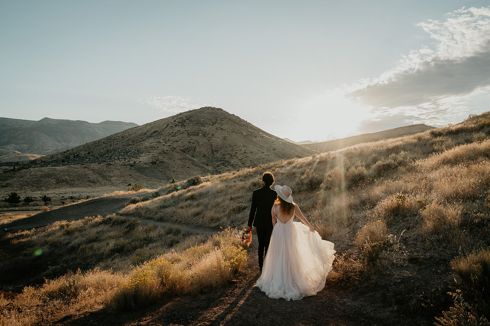 newlyweds enjoying the sunrise while standing in a meadow. 