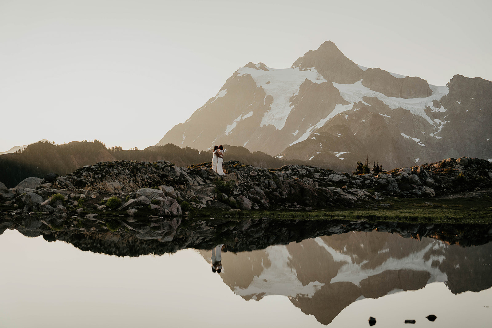 Newlyweds standing by an alpine lake as they elope at sunrise. 