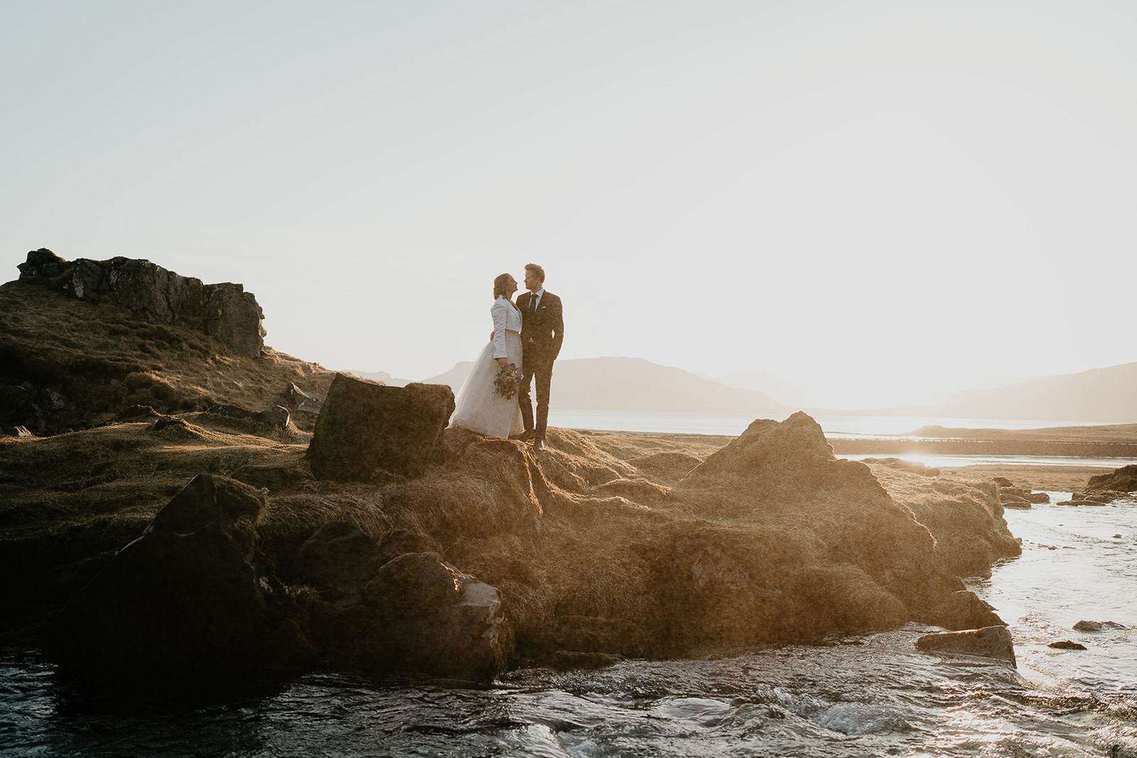 newlyweds hugging as they stand by the coast.