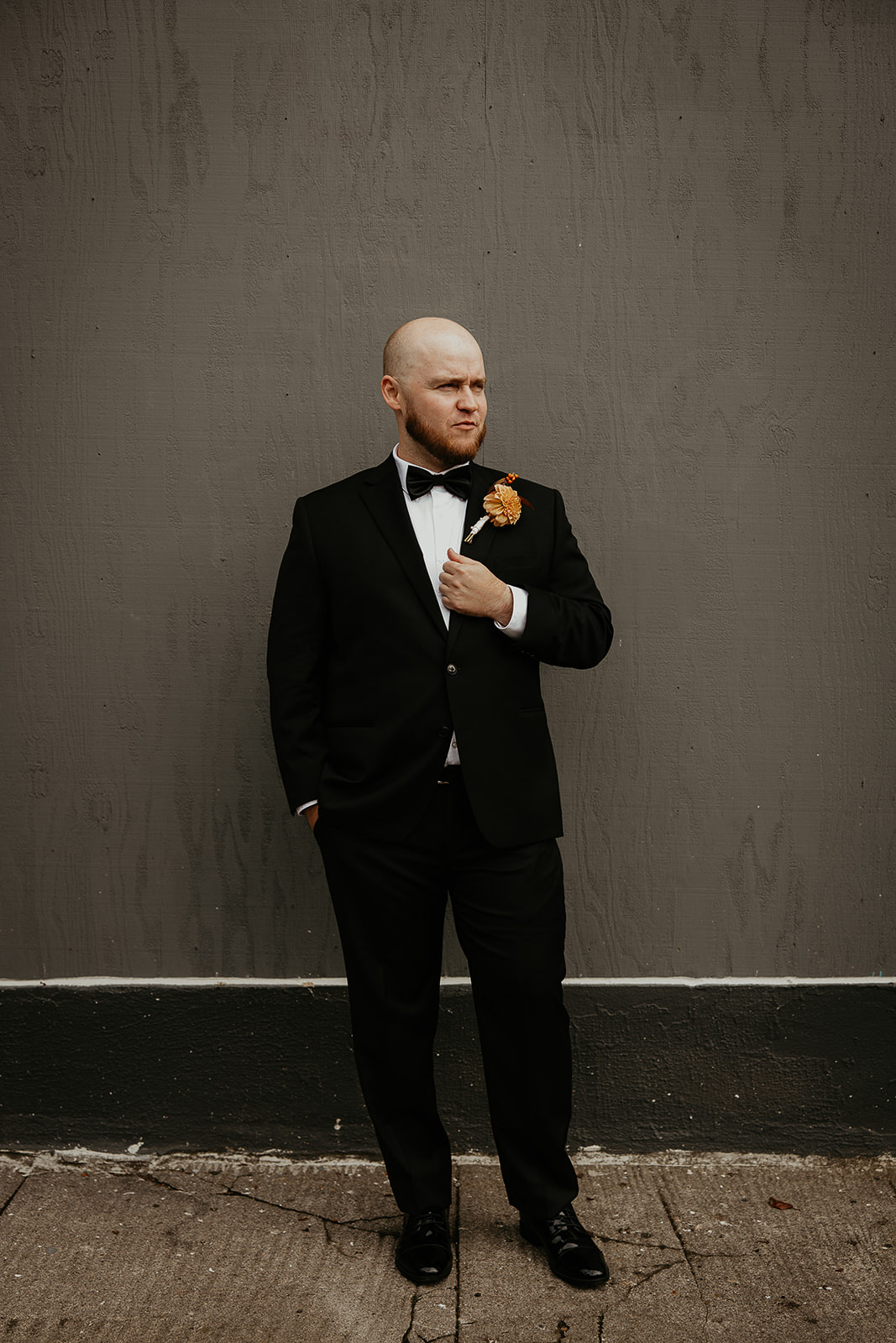 groom posing next to a gray wall.