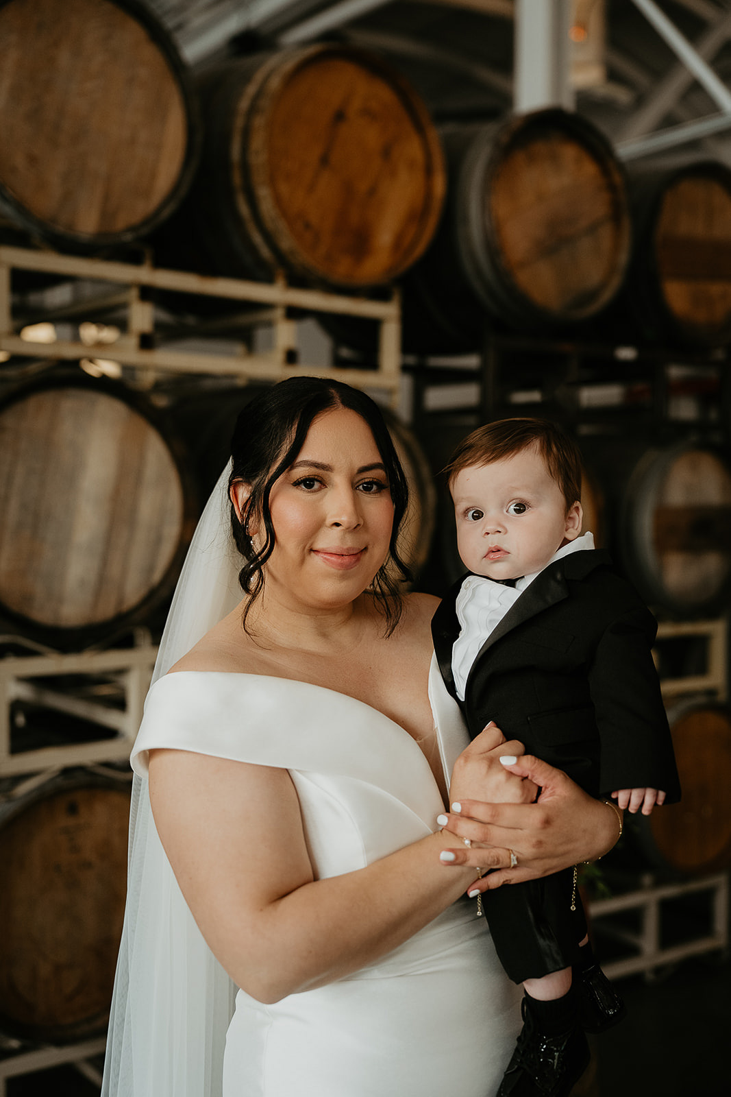 bride holding her son in front of wine barrel during their Coopers Hall wedding.