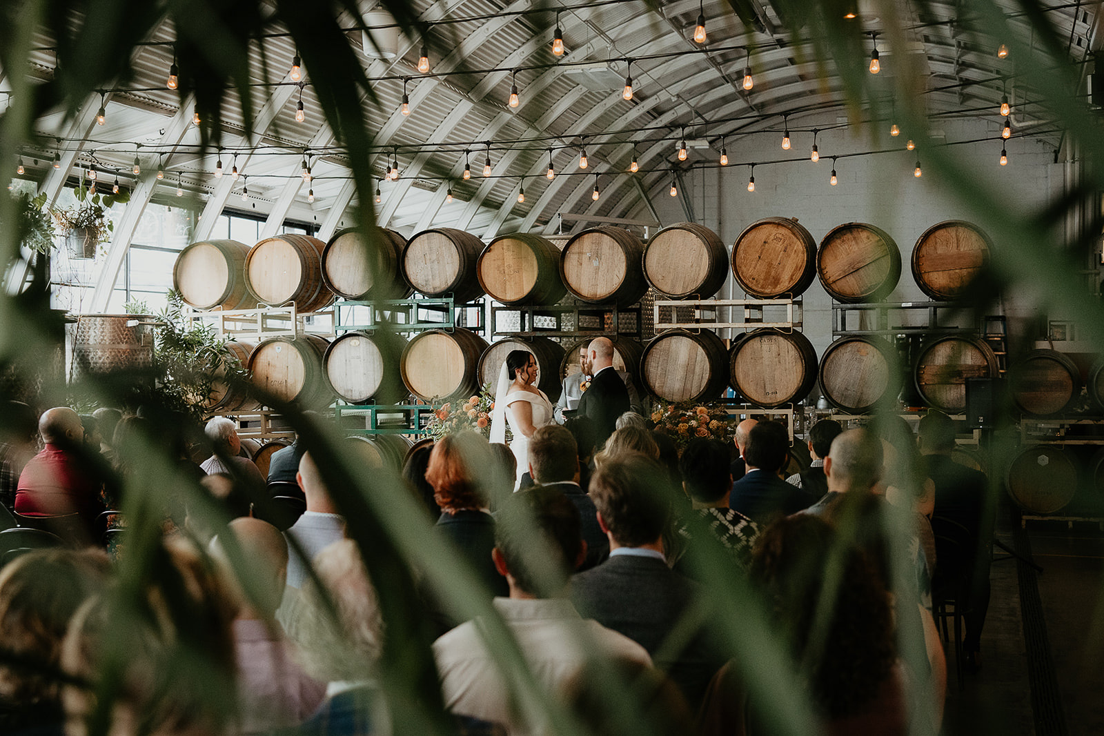 newlyweds holding their wedding ceremony at coopers with wine barrels behind them.