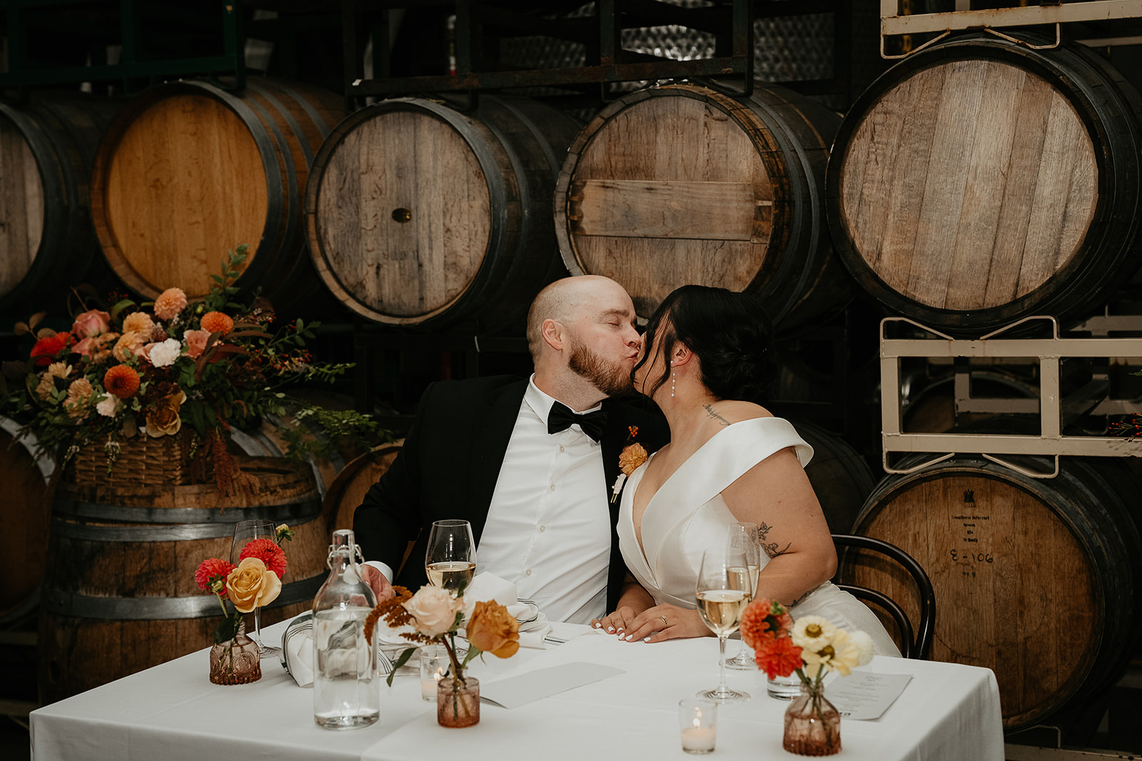 newlyweds kissing behind several wine barrels.