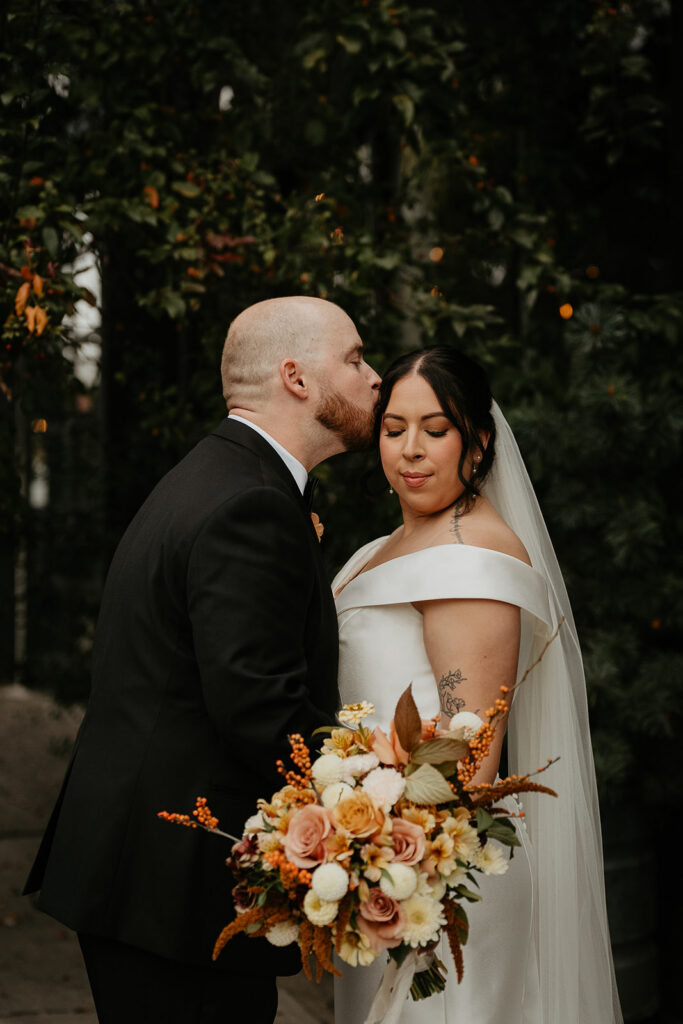 the husband kissing the birde, while she holds a bouquet of flowers during their Coopers Hall wedding.