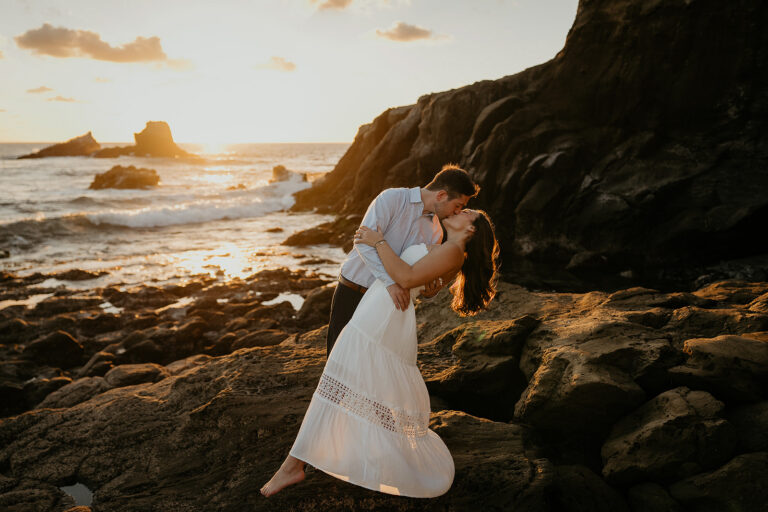 couple kissing at sunset on a rocky shoreline during their Laguna Beach engagement.