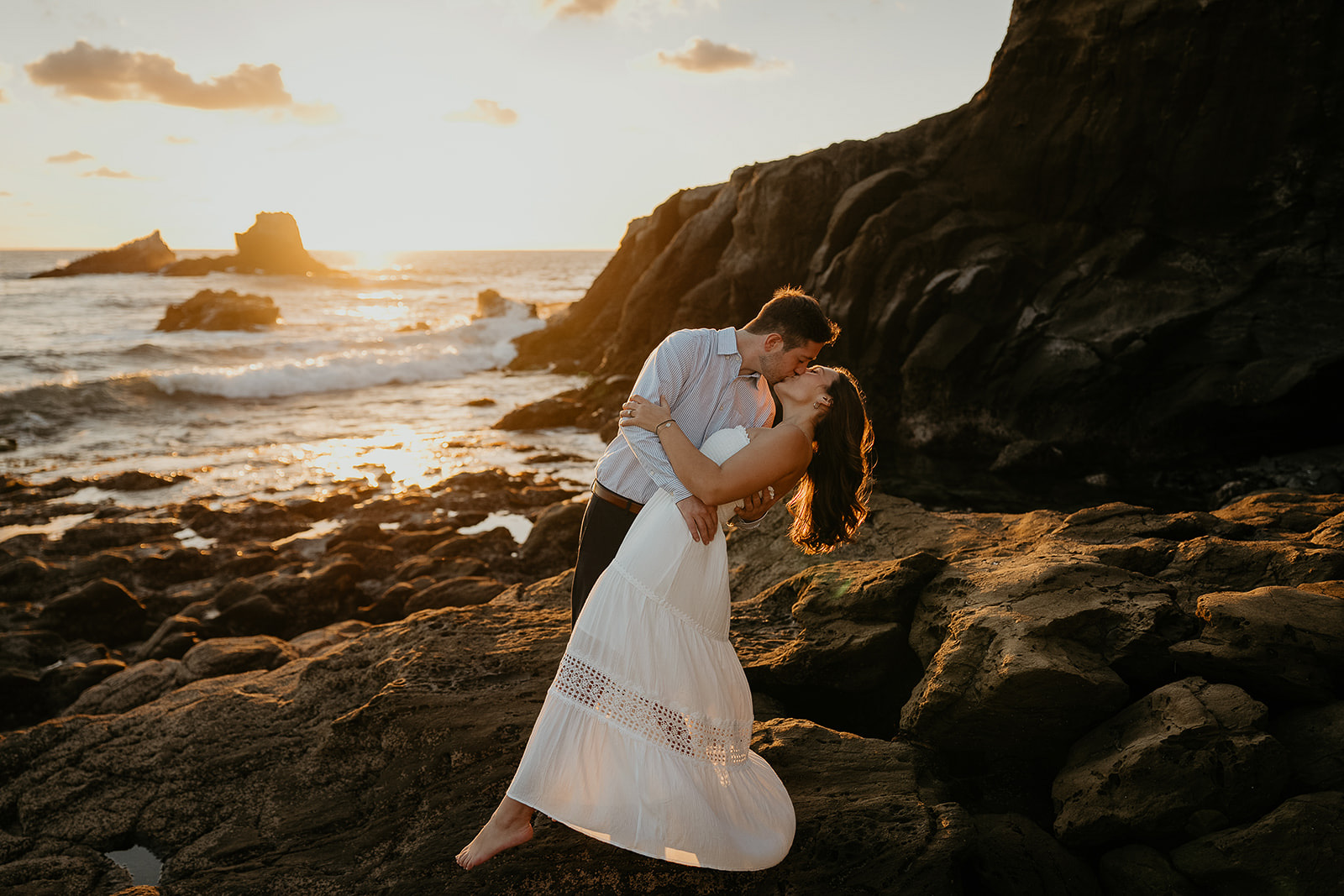 couple kissing at sunset on a rocky shoreline during their Laguna Beach engagement.
