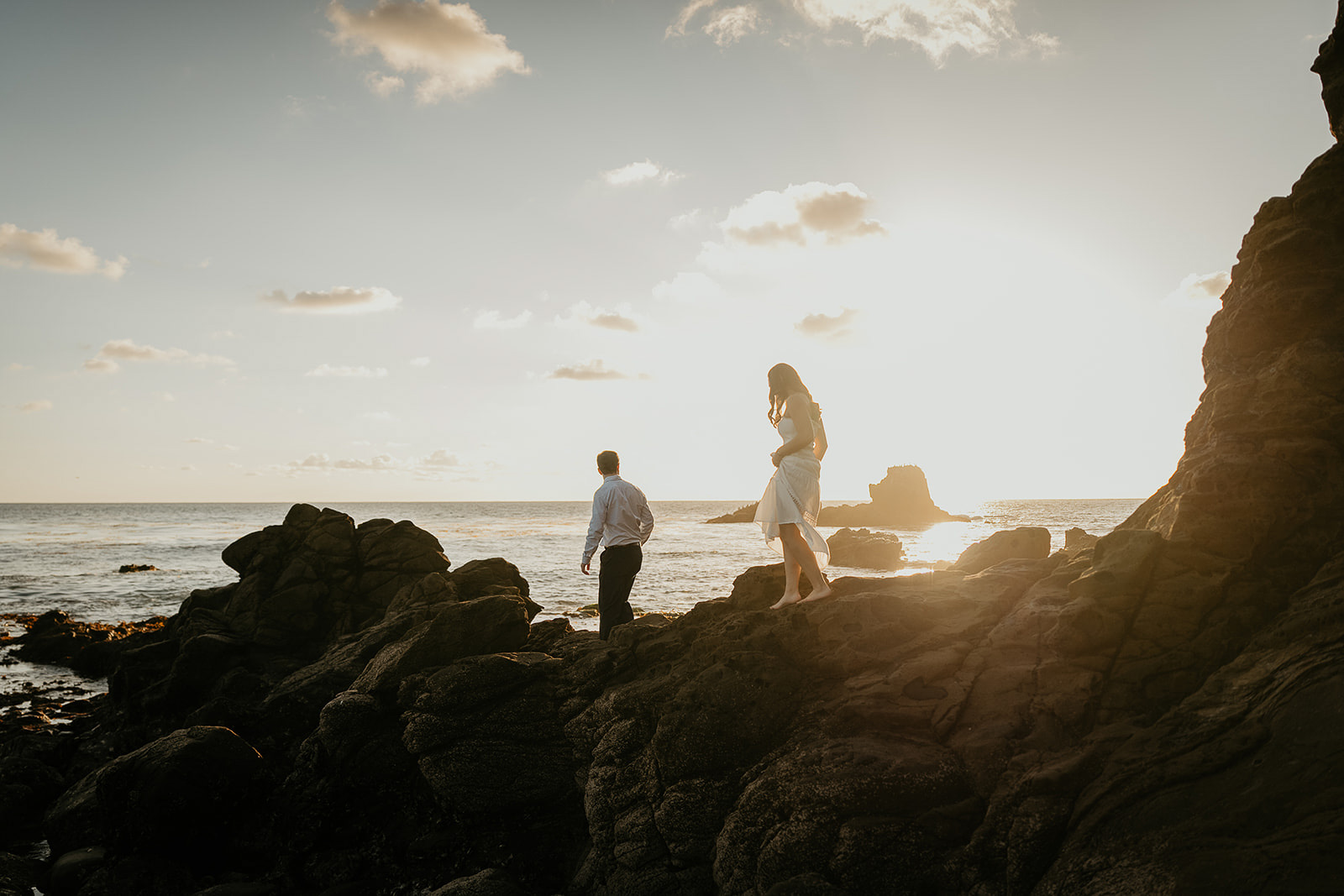 couple walking along a rocky cliff by the ocean during their Laguna Beach engagement.