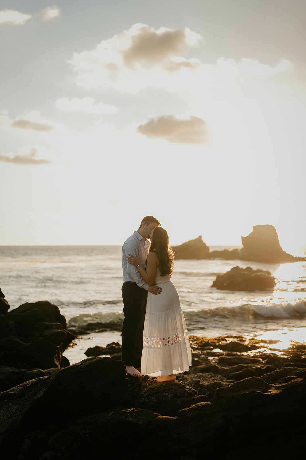 couple hugging and kissing standing on rocks by the ocean during their Laguna Beach engagement.