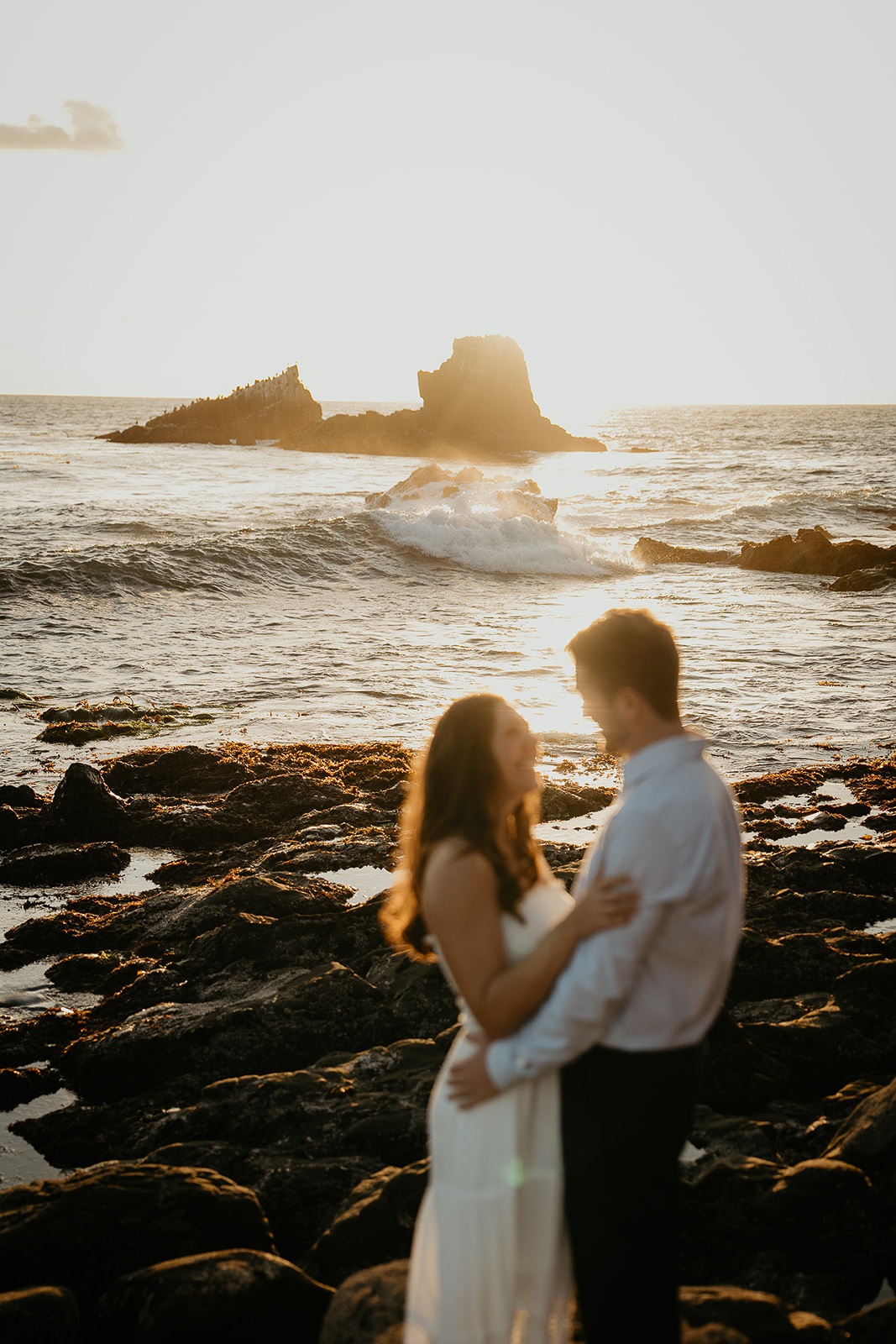 couple hugging with the ocean and the sun setting behind them.