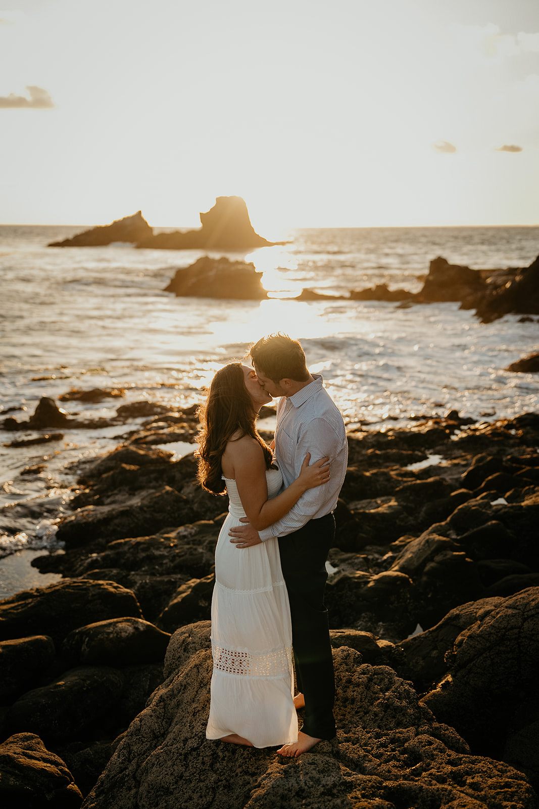 couple kissing on the rocky shoreline at sunset during their Laguna Beach engagement.