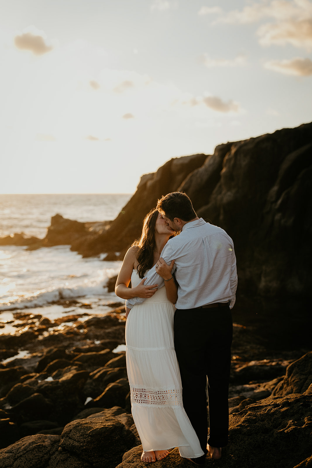 couple kissing while standing on a rock next to the ocean during their Laguna Beach engagement.