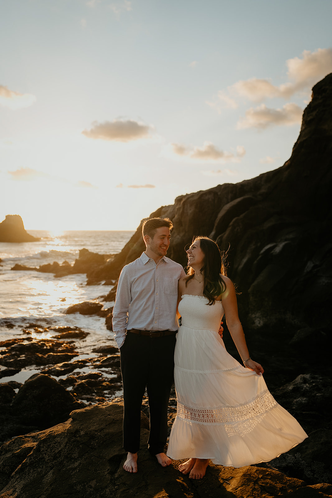 couple holding each other and smiling with the ocean behind them.
