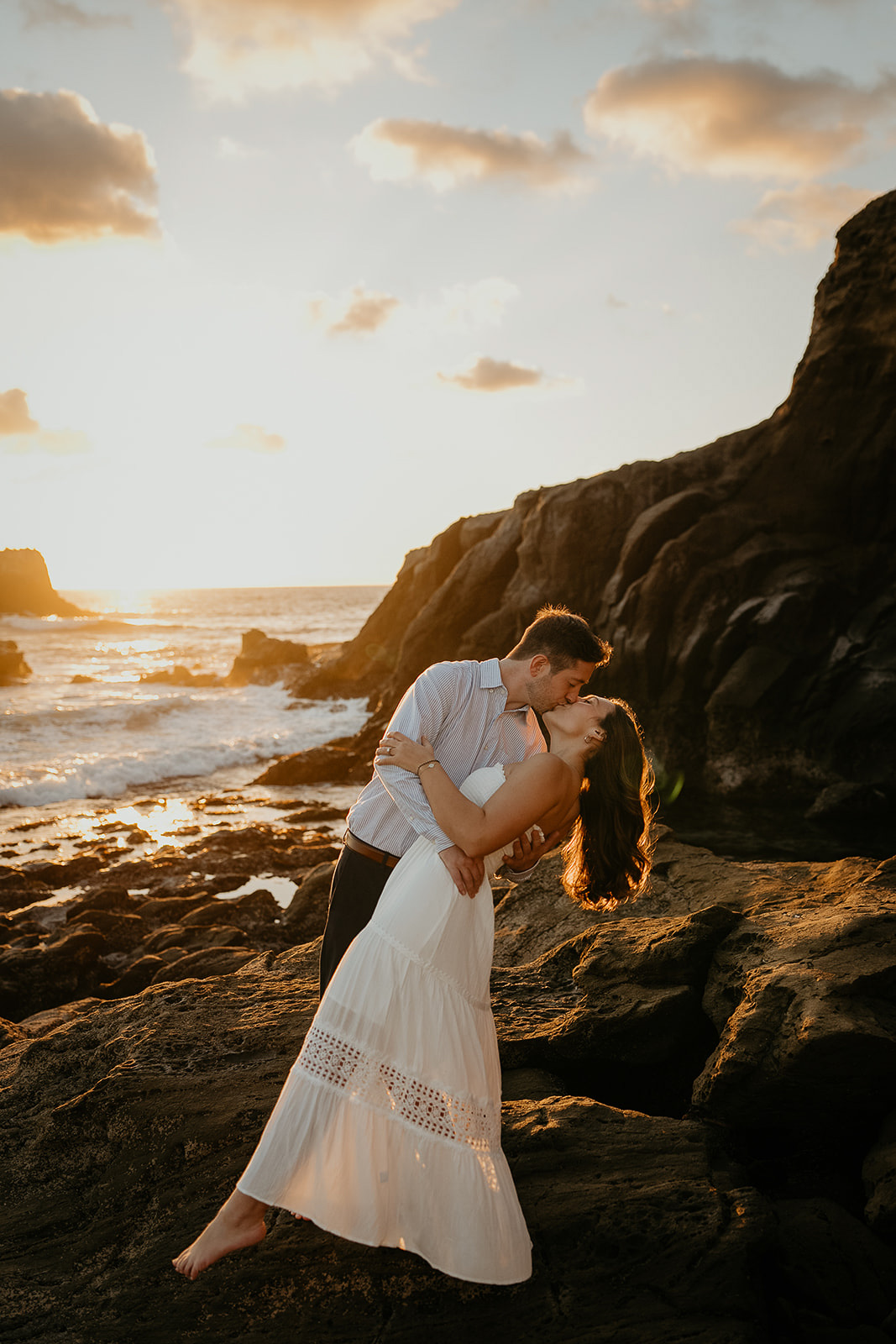 couple kissing while standing on a rock at sunset by the ocean during their Laguna Beach engagement.