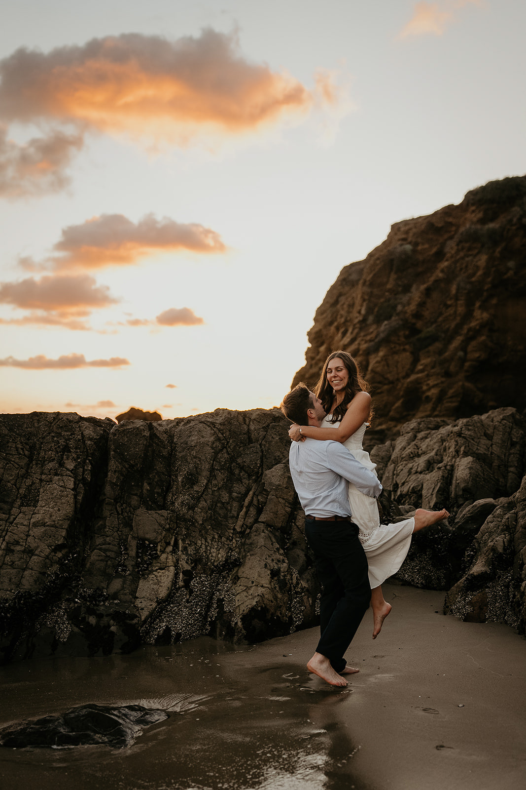 couple hugging on the beach by several large rocks during their Laguna Beach engagement.