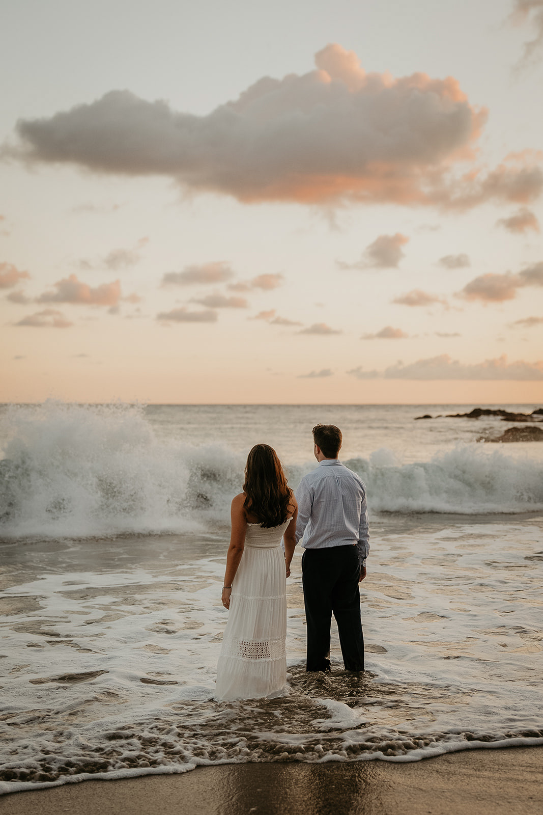 couple standing in the surf looking out over the pacific ocean during their Laguna Beach engagement.