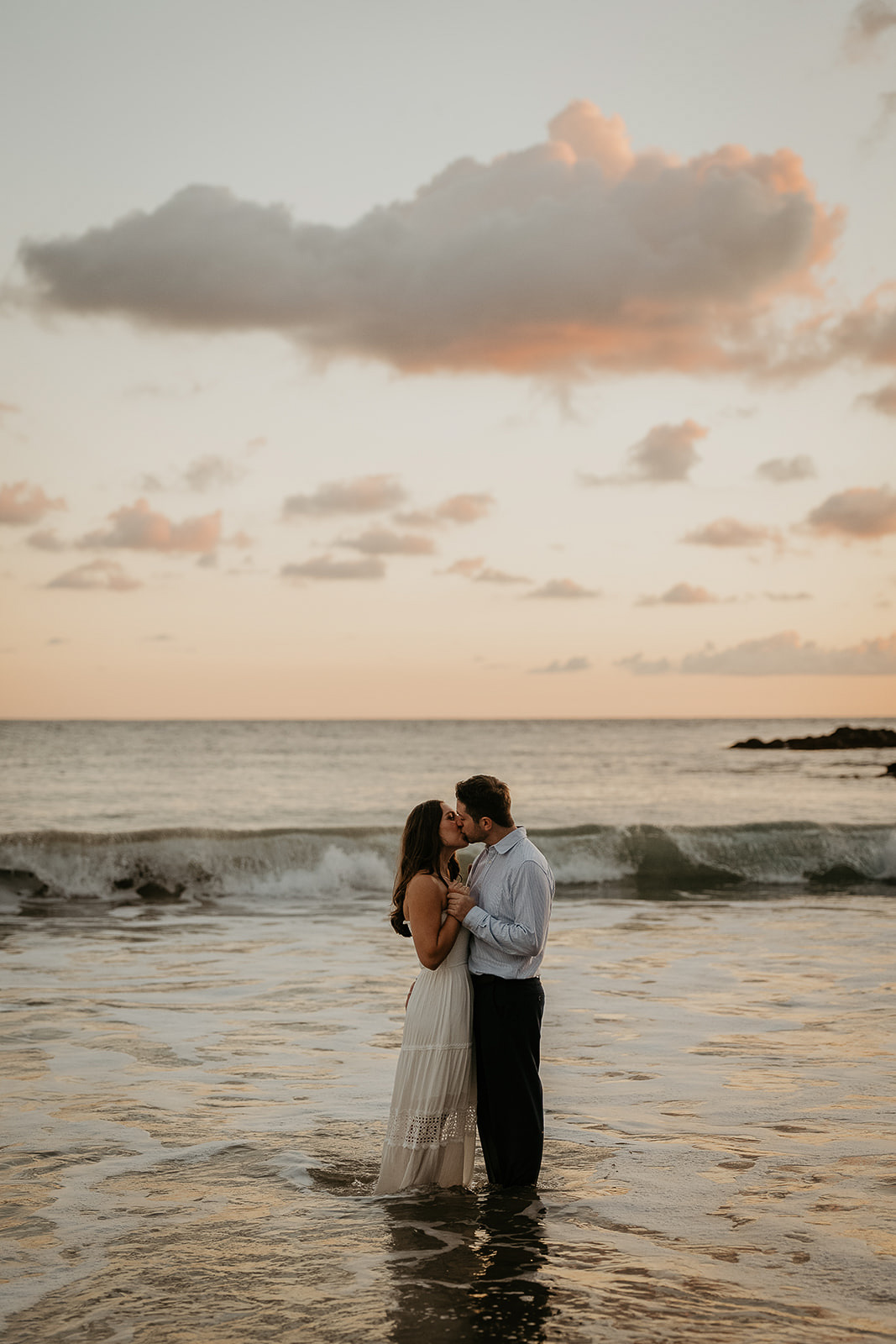 couple standing in the surf kissing at sunset.