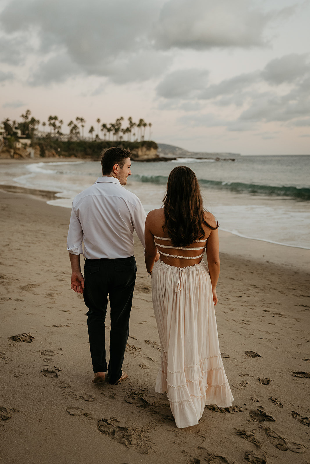 couple holding hands walking on the sand during their Laguna Beach engagement.