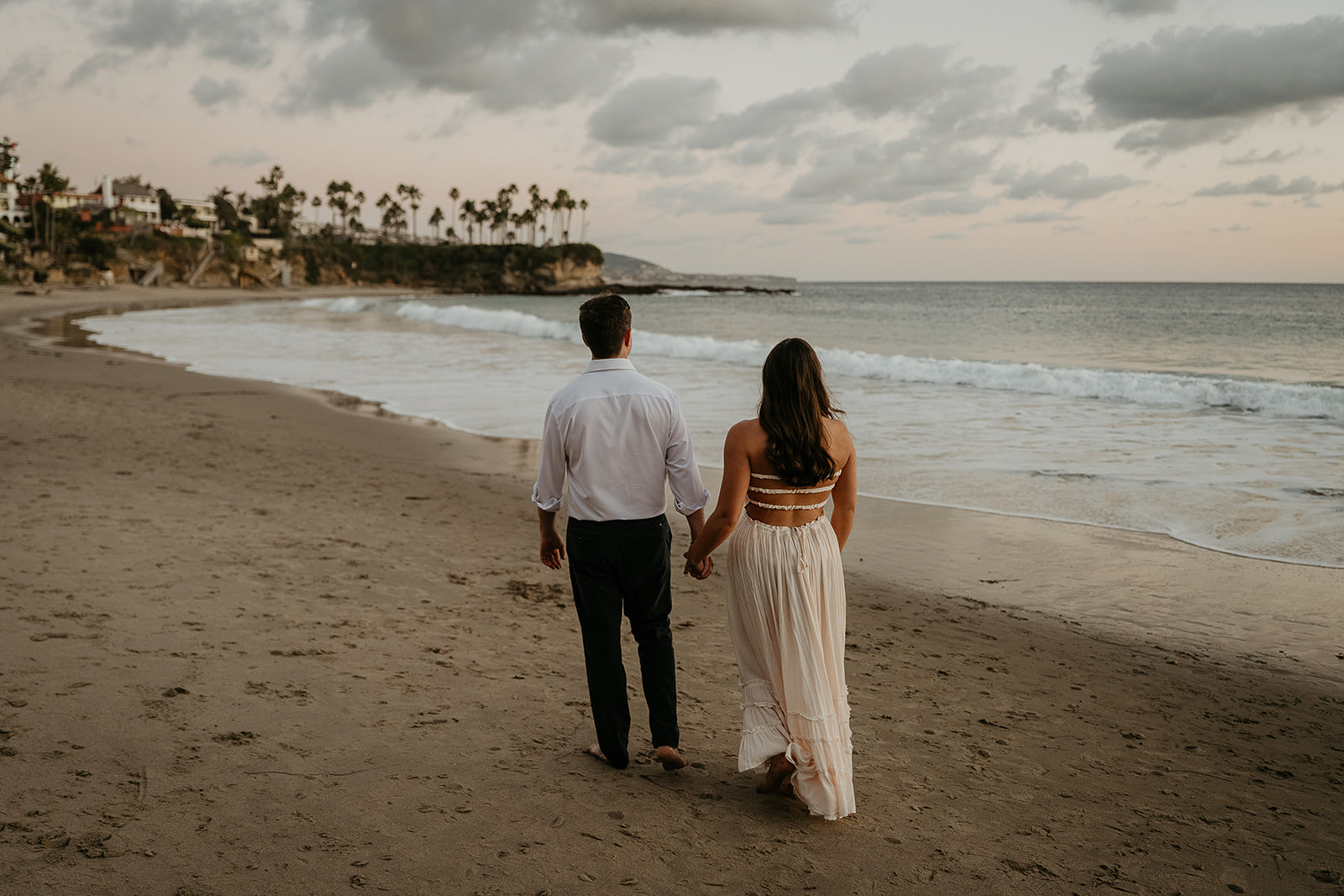 couple holding hands walking on the sand during their Laguna Beach engagement.