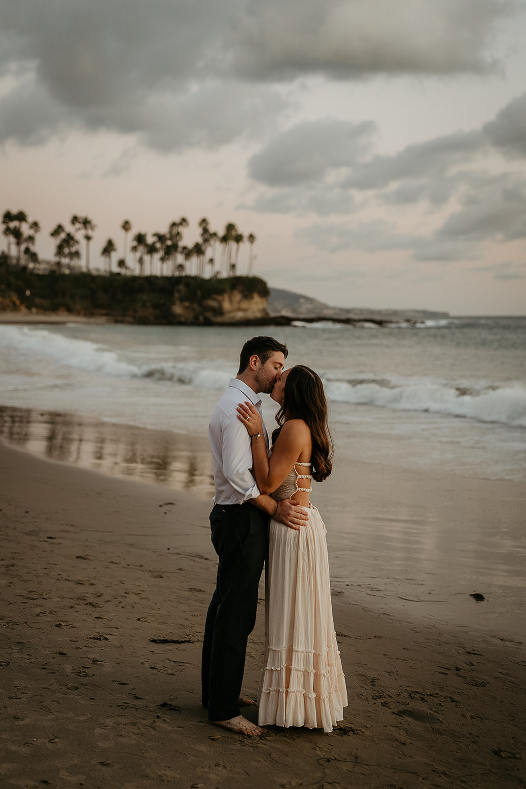 couple kissing on the sand with waves crashing behind them during their Laguna Beach engagement.