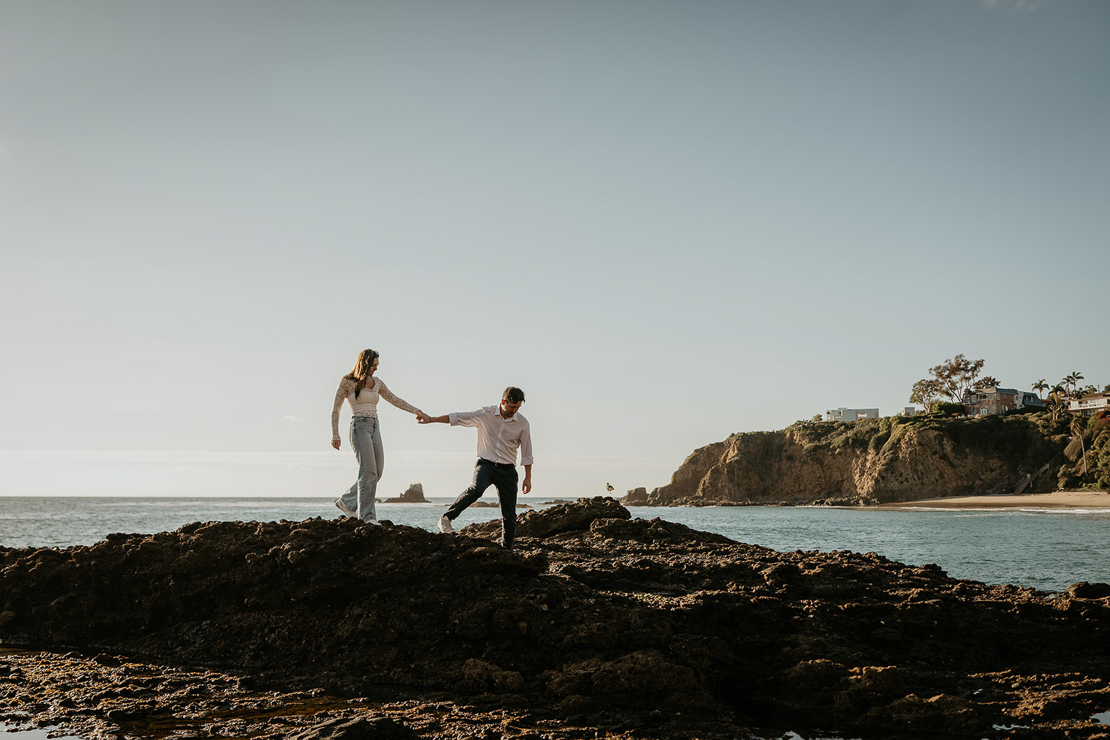couple walking on the rocky shoreline during their Laguna Beach engagement.