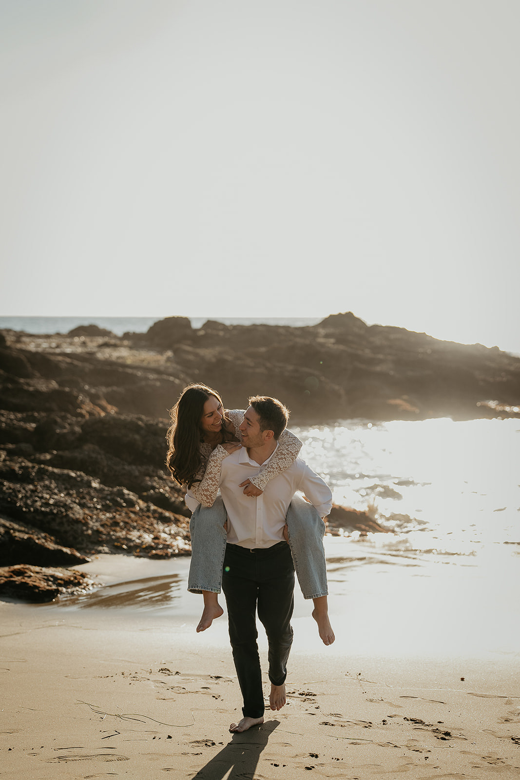 couple piggybacking on the sand during their Laguna Beach engagement.