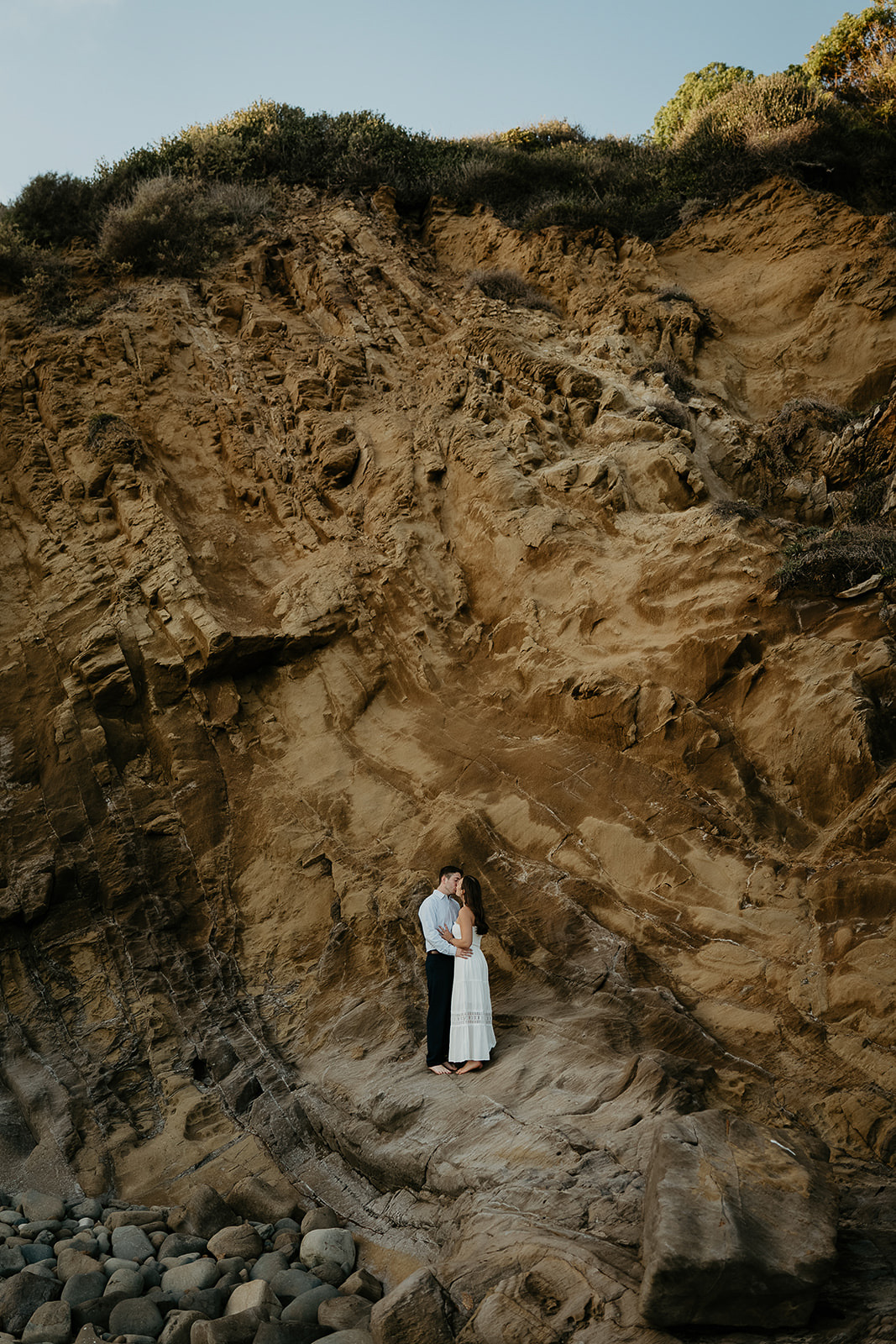 couple standing next to a large ocean cliff kissing during their Laguna Beach engagement.