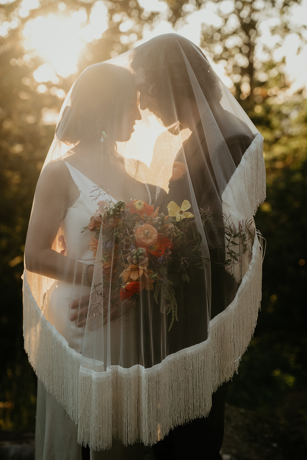 the newlyweds holding each other under the bride's veil during their vintage inspired wedding.