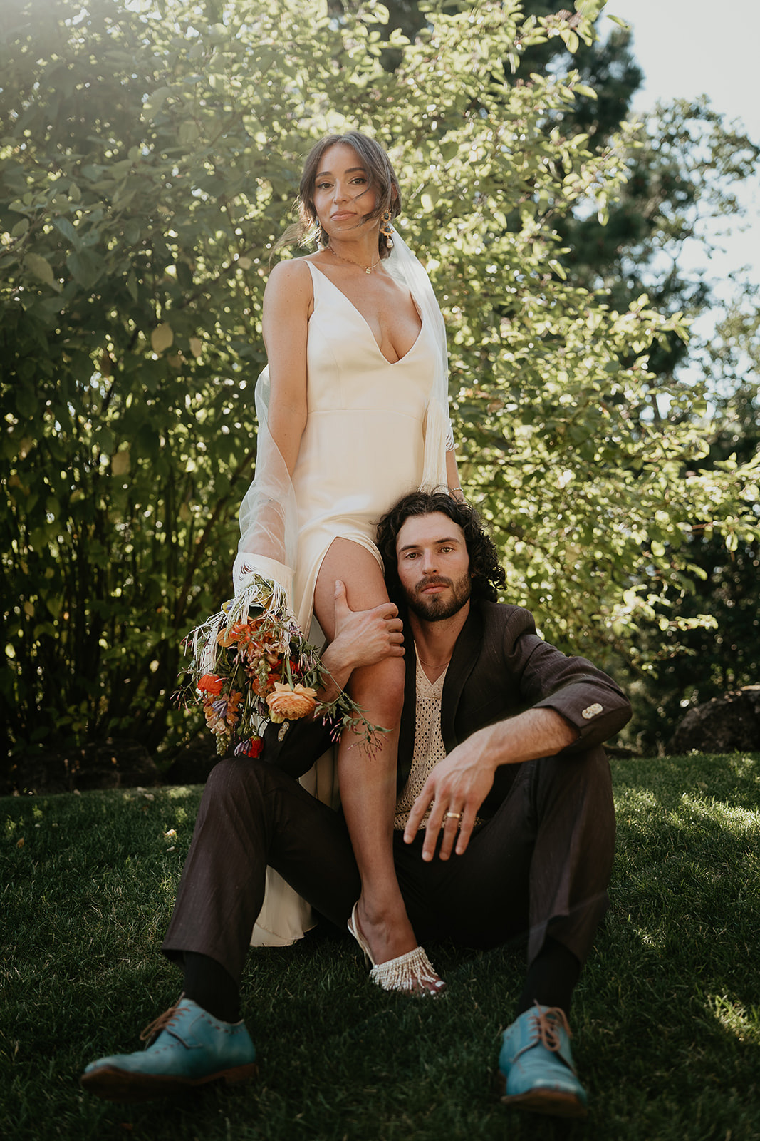 the bride resting her leg over her groom's shoulder while he sits on the grass during their vintage inspired wedding.