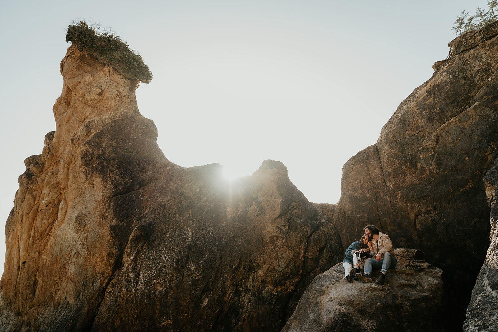 couple hugging while sitting on a rock with their dog.