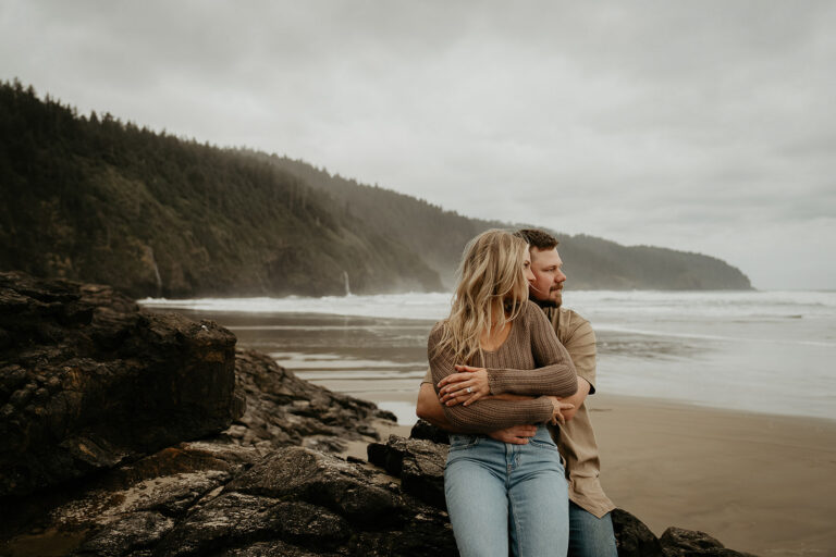 couple hugging while sitting on a rock on the Oregon coastline.
