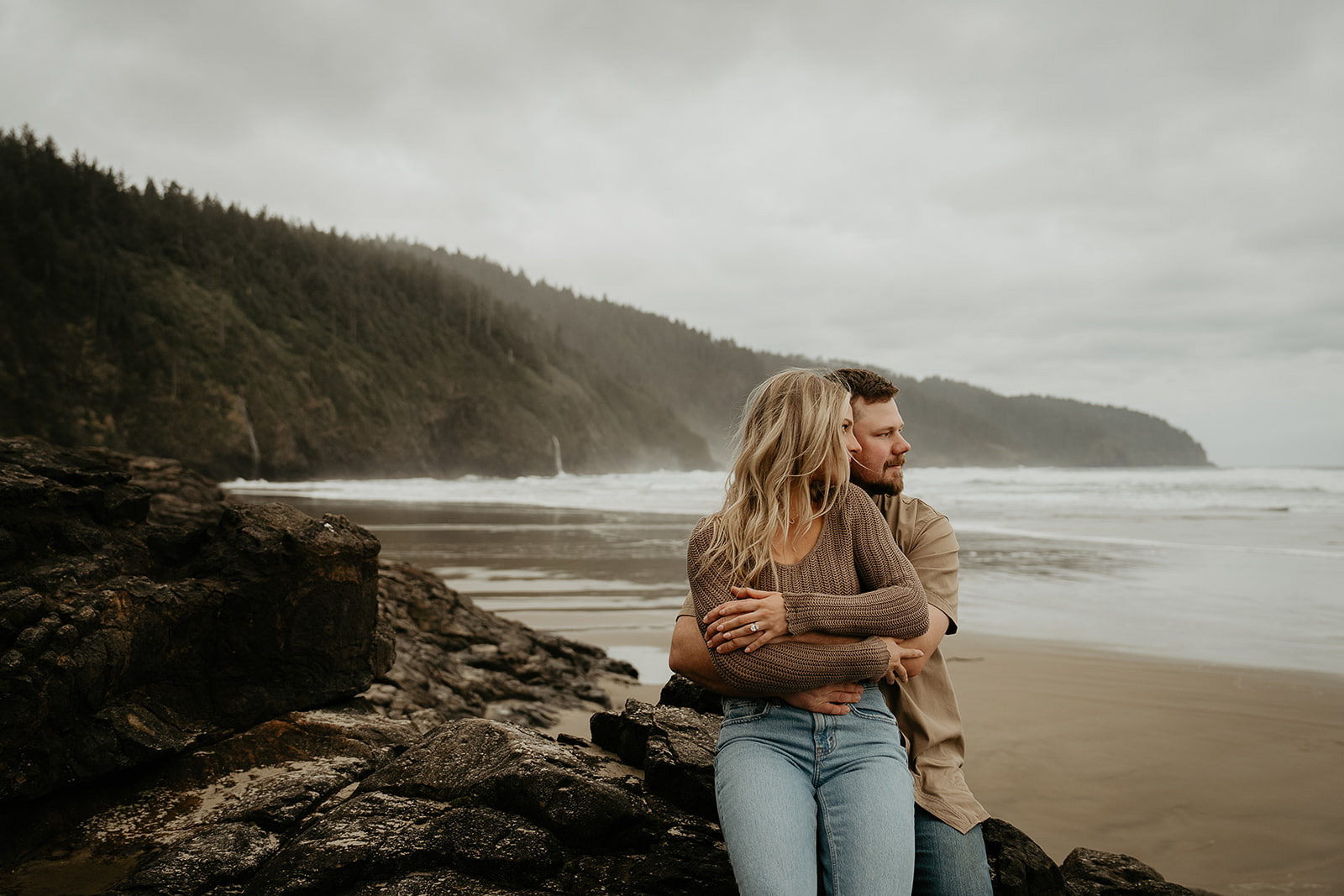 couple hugging while sitting on a rock on the Oregon coastline.