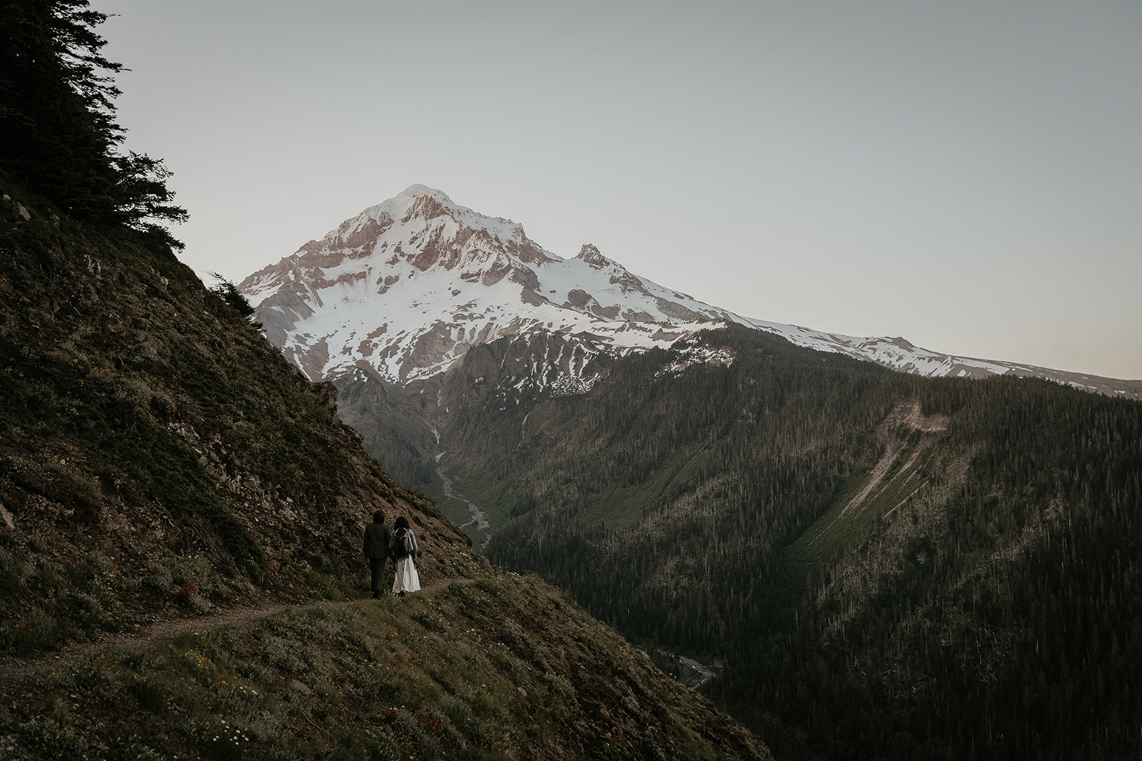 couple walking along a hiking trail with mount Hood during their wedding anniversary photoshoot.