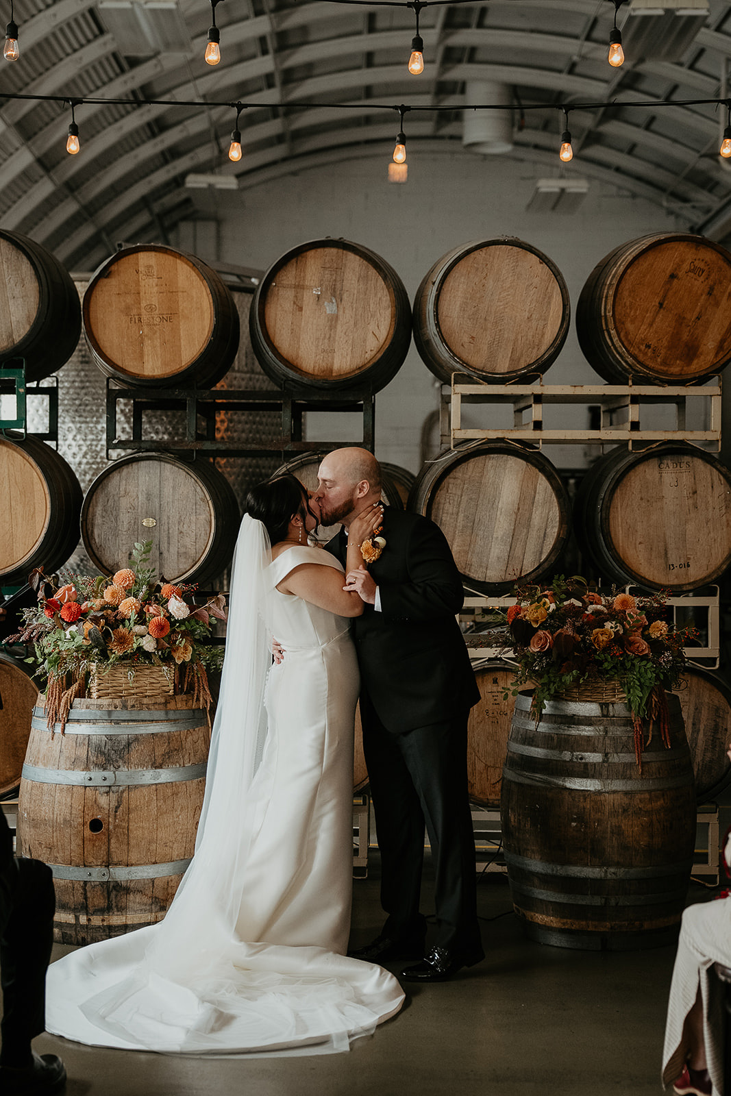 Newlyweds kissing in front of wine barrels.